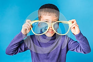Cheerful little boy in big glasses express a surprised face isolated on blue background.