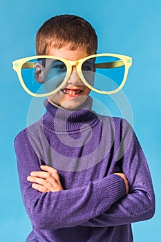 Cheerful little boy in big glasses express a surprised face isolated on blue background.