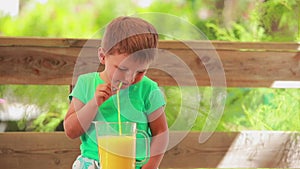 The cheerful little boy is drinking fresh orange juice with a straw