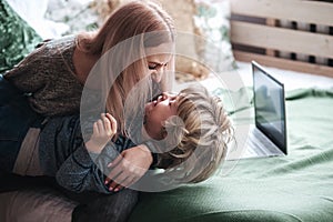 Cheerful little boy having fun with mother on sofa