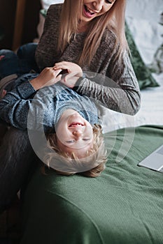 Cheerful little boy having fun with mother on sofa