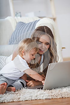 Cheerful little boy and his mother lying on the floor while playing game on the laptop