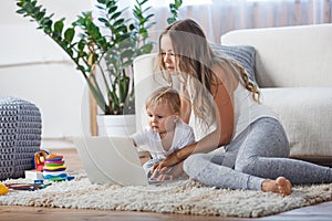 Cheerful little boy and his mother lying on the floor while playing game on the laptop