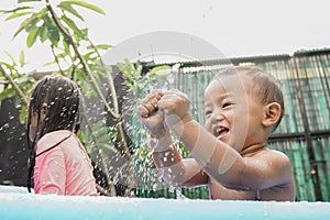 cheerful little boy playing water in the outdoor pool with sibling