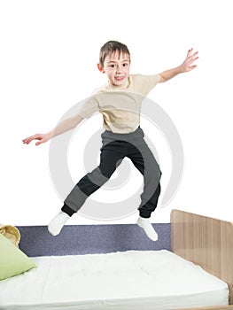 Cheerful little boy in a shirt and trousers jumping on the bed and waves his hands