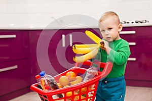 Cheerful little boy with shopping cart. Little boy takes bananas. Shopping, discount, sale concept