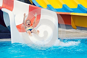 Cheerful little boy sliding into water in aqua park