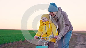 cheerful little child with her mother learns ride two-wheeled bike sunset, happy family, pedal and wheel, mom help kid