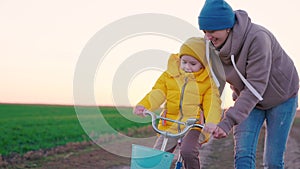 cheerful little child with her mother learns ride two-wheeled bike sunset, happy family, pedal and wheel, mom help kid