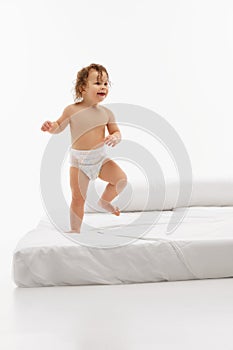 Cheerful little child, small kid, girl with wet hair in standing pose playing on bed against bright white studio
