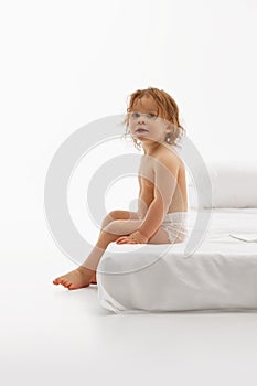 Cheerful little girl, baby with wet curly hair siting in cozy, comfortable bedroom against white background. Textile for