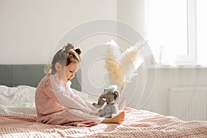 A cheerful little girl on the bed after waking up plays with her toy elephant