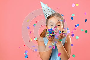 Cheerful little girl celebrates birthday. The child blows confetti from the hands. Closeup portrait on pink coral background