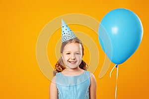 Cheerful little girl celebrates birthday. A child holds a blue balloon and looks into the camera.