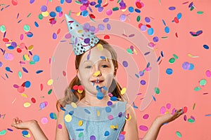 Cheerful little girl celebrates birthday. A child is standing in a rain of confetti. A party. Closeup portrait on pink background