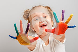 Cheerful little girl child shows hands painted with paint. Gray background, portrait