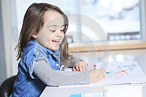 Cheerful little girl colouring at the table at