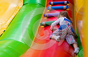 A cheerful little girl is having fun on a high inflatable game slide. A little baby is playing on an inflatable trampoline on a fe