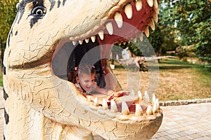 Cheerful little girl having fun in park with dinosaur replicas outdoors