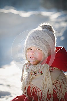 Cheerful little girl in a knitted hat, red coat and a beautiful shawl