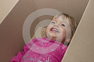 A cheerful little girl lies in a cardboard box and smiles. Concept: children`s fantasy and toys, Playhouse and family.