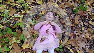 Cheerful little girl lies on fallen autumn leaves