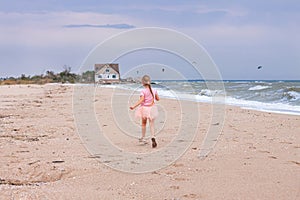 Cheerful little girl with long blonde hair in pink tulle skirt walking empty sea beach alone. Beautiful little princess