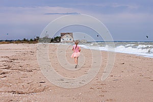 Cheerful little girl with long blonde hair in pink tulle skirt walking empty sea beach alone. Beautiful little princess