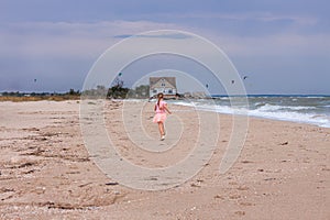 Cheerful little girl with long blonde hair in pink tulle skirt walking empty sea beach alone. Beautiful little princess