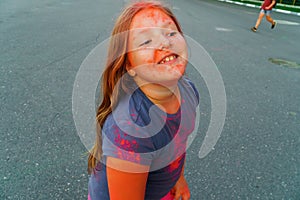 Cheerful little girl with long hair covered pink and purple dry paint Holi