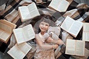 Cheerful little girl lying on floor with lot of books;