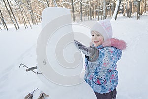 Cheerful little girl making three ball snowman from snow