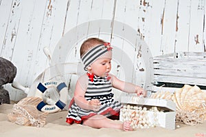 Cheerful little girl in a marine style sits on the sand