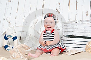 Cheerful little girl in a marine style sits on the sand