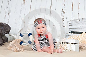 Cheerful little girl in a marine style sits on the sand