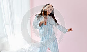 Cheerful little girl in pajama on the bed holding a hair brush like microphone singing imitates herself a real singer in the