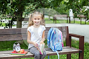 A cheerful little girl is reading a book on a bench. The concept of school, study, education, friendship, childhood.