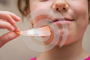 A cheerful little girl removes a sticky patch from her skin. Children`s mouth close-up.Child pulling the plaster off his face