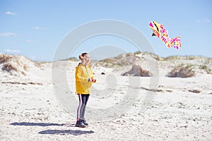 Cheerful little girl running in dress on beach with kite
