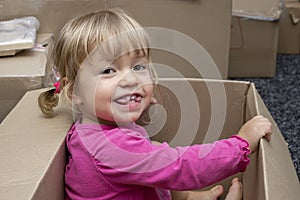 A cheerful little girl sits in a cardboard box and smiles. Concept: children`s fantasy and toys, Playhouse and family.