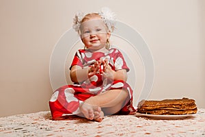 A cheerful little girl sits on a table and tastes festive pancakes. shrovetide