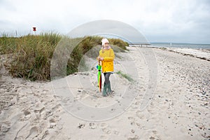 Cheerful little girl staying on beach with colorful ambrella on Baltic sea at rainy weather