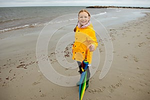 Cheerful little girl staying on beach with colorful ambrella on Baltic sea at rainy wether photo