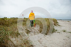 Cheerful little girl staying on beach with colorful ambrella on Baltic sea at windy rainy weather photo