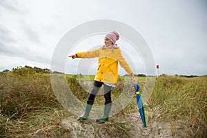 Cheerful little girl staying on beach with colorful ambrella on Baltic sea at windy rainy weather photo