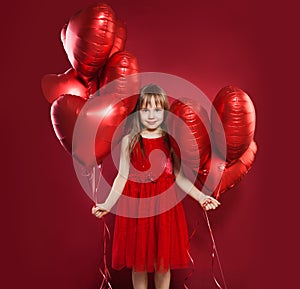 Cheerful little girl in tulle skirt holding balloons red heart on red background. Celebrating brightful carnival for kids