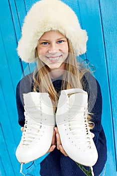 Cheerful little girl in warm sweater and hat keeps figure skates