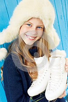 Cheerful little girl in warm sweater and hat keeps figure skates