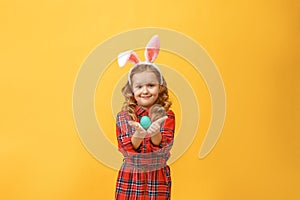 Cheerful little kid girl with bunny ears with an easter egg on a colored background