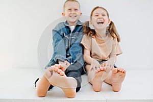 Cheerful little siblings sitting on a table with bare feet. Both laughing.